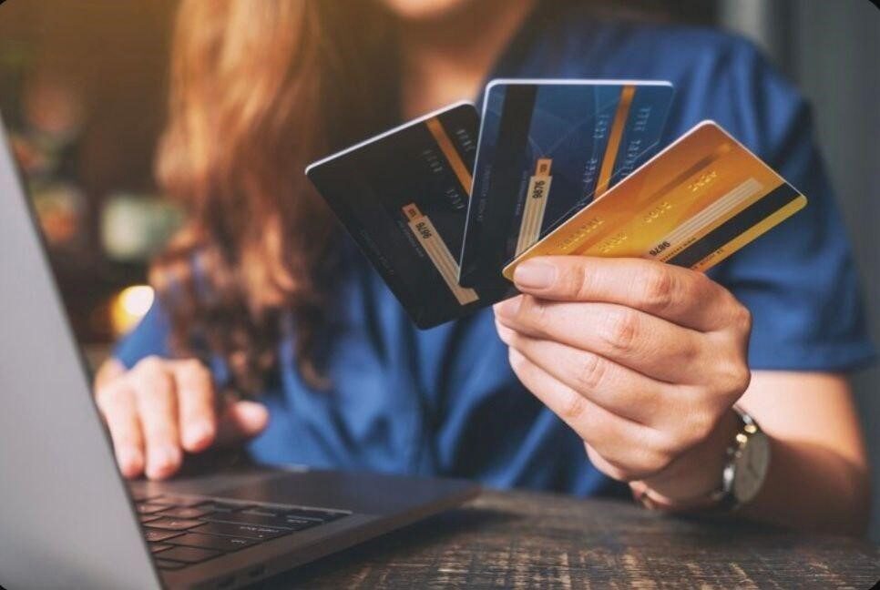 فردی در حال استفادهاز لپ تاپ و نگه داشتن چند کارت اعتباری با رنگهای مختلف