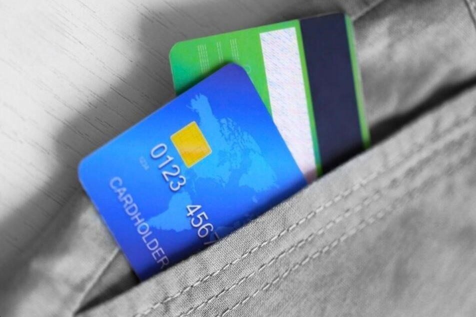 دو کارت اعتباری با رنگهای آبی و سبز داخل جیب شلوار خاکستری قرار گرفتهاند.